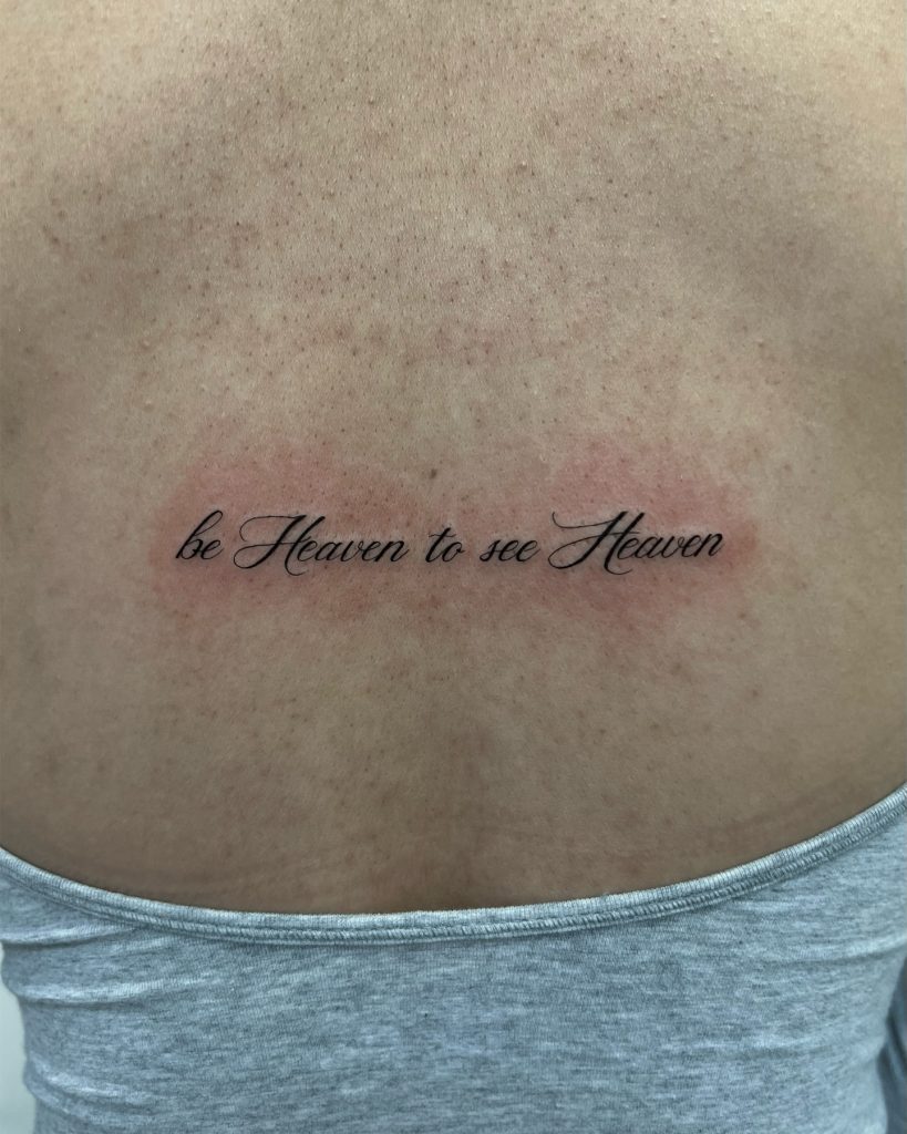 dainty text tattoo on the back reads "be heaven to see heaven"